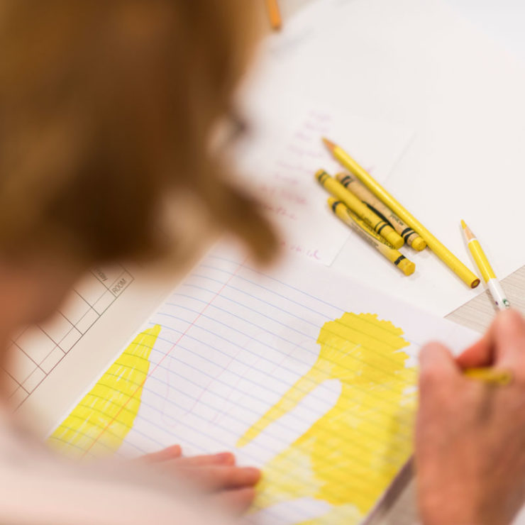 A Drawing Gym Participants Leans Over Her Notebook And Uses Yellow Crayons Markers And Colored Pencils