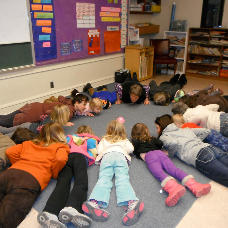 Children lying on their stomachs in a circle to depict a Kindness Curriculum practice.